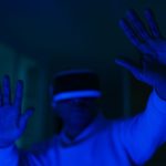 Homem usando um headset de realidade virtual e interagindo com as mãos em um ambiente iluminado por luz azul.