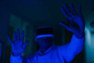 Homem usando um headset de realidade virtual e interagindo com as mãos em um ambiente iluminado por luz azul.