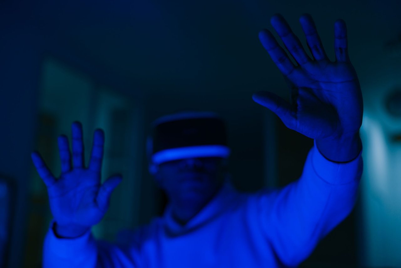 Homem usando um headset de realidade virtual e interagindo com as mãos em um ambiente iluminado por luz azul.